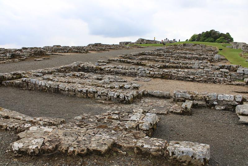 Housesteads Roman Fort 4 Ancient stone ruins with low walls on a slightly hilly terrain under a cloudy sky.